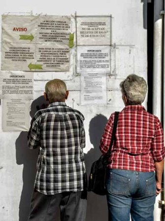 14 DE ENERO: Dos cubanos reciben información en un mural sobre la nueva ley migratoria mientras solicitan visas en la embajada de México en La Habana.