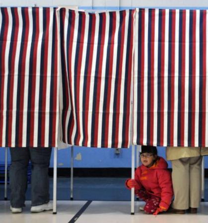 Una niña observa por debajo del cubículo mientras su madre emite su voto en Manchester, New Hampshire.