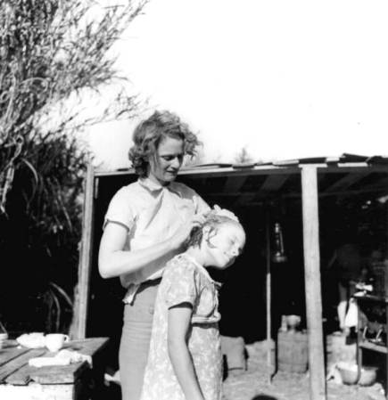 Trabajadora de la planta de empaque de Tennessee, limpiando el estiércol húmedo y negro del cuero cabelludo de su hija, lo que provoca una erupción cutánea con picor y llagas y costras en el cuero cabelludo, El agua es sucia de un canal cercano - Belle Glade, Florida, 1939.