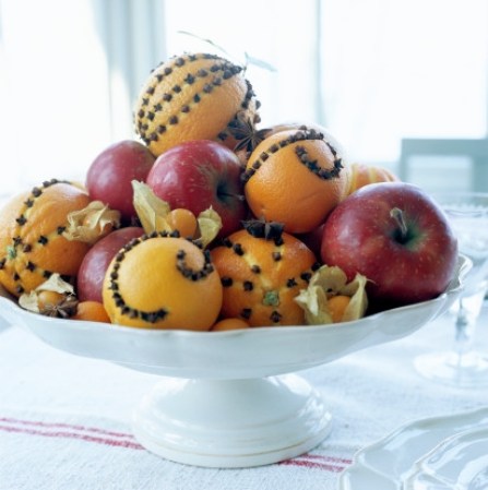 Utiliza frutas como la naranja y la manzana decoradas con clavos para un centro de mesa.