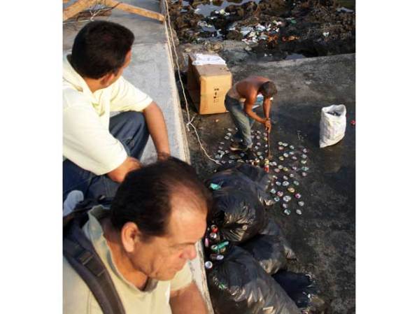Un hombre mete latas de aluminio en una bolsa, para venderlas.