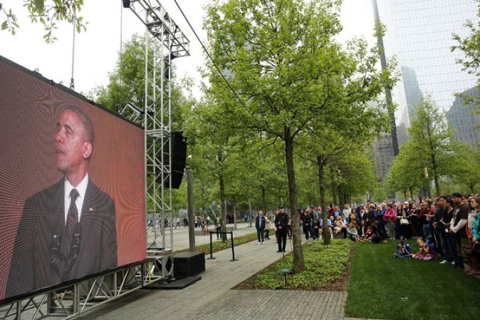 NEW YORK, NY - MAY 15: People watch a live video from the Ground Zero memorial site of the dedication ceremony of the National September 11 Memorial Museum in New York May 15, 2014 in New York City. The museum spans seven stories, mostly underground, and contains artifacts from the attack on the World Trade Center Towers on September 11, 2001 that include the 80 ft high tridents, the so-called "Ground Zero Cross," the destroyed remains of Company 21's New York Fire Department Engine as well as smaller items such as letter that fell from a hijacked plane and posters of missing loved ones projected onto the wall of the museum. The museum will open to the public on May 21. (Photo by Spencer Platt/Getty Images)