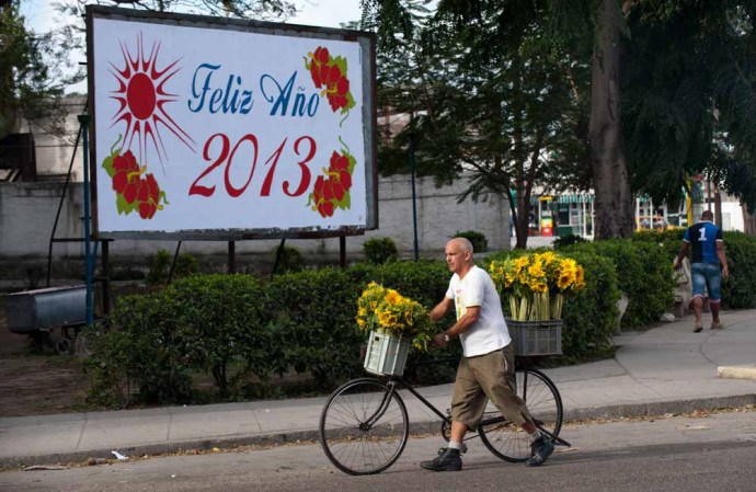 30 DE DICIEMBRE DE 2012: Un vendedor de flores camina frente a una valla en La Habana que publicita la llegada del año nuevo.