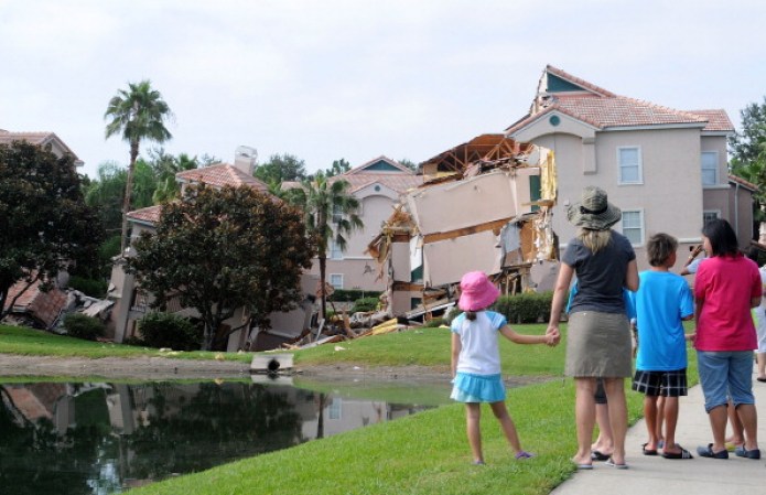 CLERMONT, FL - AUGUST 12: People look at a partially collapsed building over a sinkhole at Summer Bay Resort near Disney World on August 12, 2013 in Clermont, Florida. The 40 to 60 foot sinkhole opened up under the resort building reportedly begining late August 11 into early August 12. There were no injuries or deaths reported. (Photo by Gerardo Mora/Getty Images)