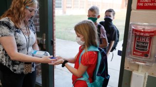 In this Aug. 5, 2020, file photo, wearing masks to prevent the spread of COVID19, elementary school students use hand sanitizer before entering school for classes in Godley, Texas.