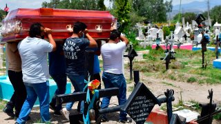 Hombres cargan un féretro en un cementerio.