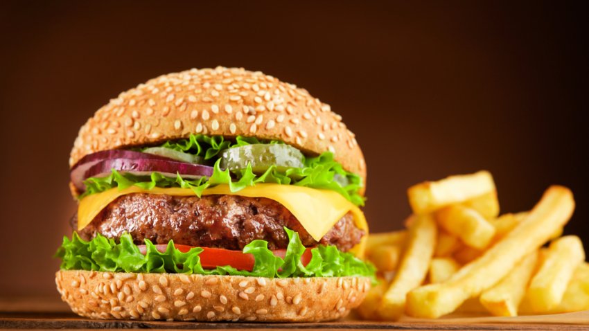 Foto de una hamburguesa de queso junto a unas papas fritas.