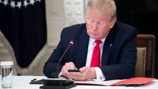 Former US President Donald Trump uses his cellphone as he holds a roundtable discussion with Governors about the economic reopening of closures due to COVID-19.