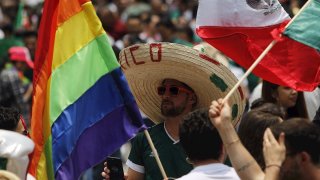 Un hombre con el típico sombrero mexicano de paja entre las banderas nacional y la del colectivo LGBTTI