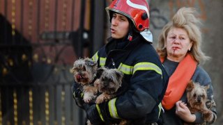 Un trabajador de emergencia lleva perros mientras escolta a un residente local fuera de un edificio de oficinas de varios pisos parcialmente destruido después de que varios ataques rusos golpearan la capital ucraniana de Kiev el 10 de octubre de 2022, en medio de la invasión rusa de Ucrania.