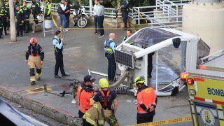 a policía y los bomberos esperan junto a un teleférico tirado en el suelo después de caer en Medellín, Colombia, el miércoles 26 de junio de 2024.