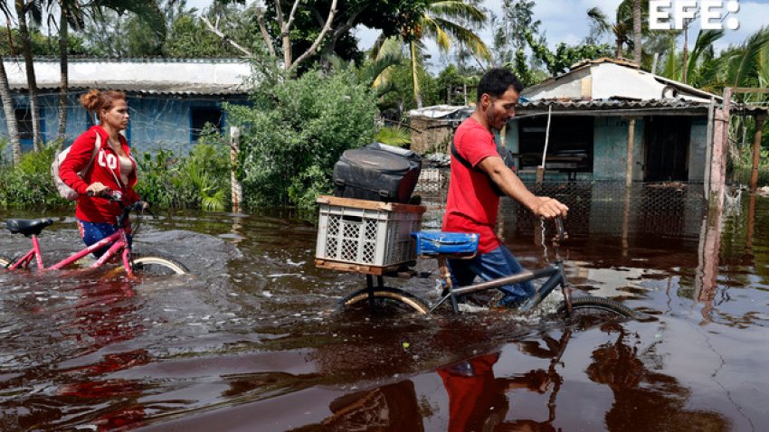 Dos personas caminan con bicicletas por una calle inundada de agua del mar este jueves, tras el paso del huracán Helen, en el poblado de Guanimar, en la costa sur de la provincia de Artemisa (Cuba). EFE/ Ernesto Mastrascusa