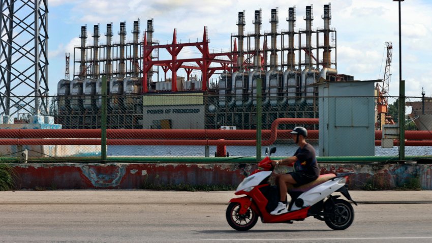 Un hombre en una moto eléctrica pasa frente a una de las plantas de generación eléctrica que permanece este domingo, en el puerto de La Habana (Cuba). EFE/ Ernesto Mastrascusa