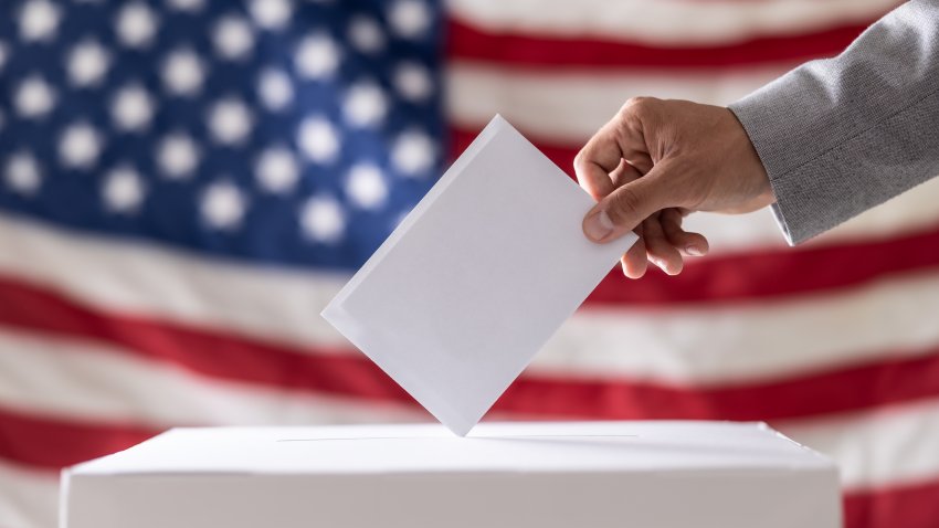 Hand holding ballot in voting ballot box with USA flag in background. USA presidential elections concept.